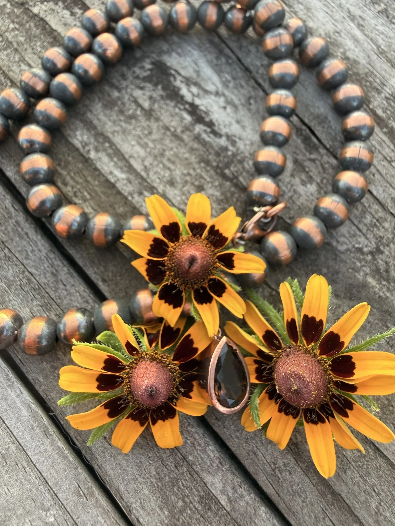 Copper-toned necklace and pendant arranged with wildflowers