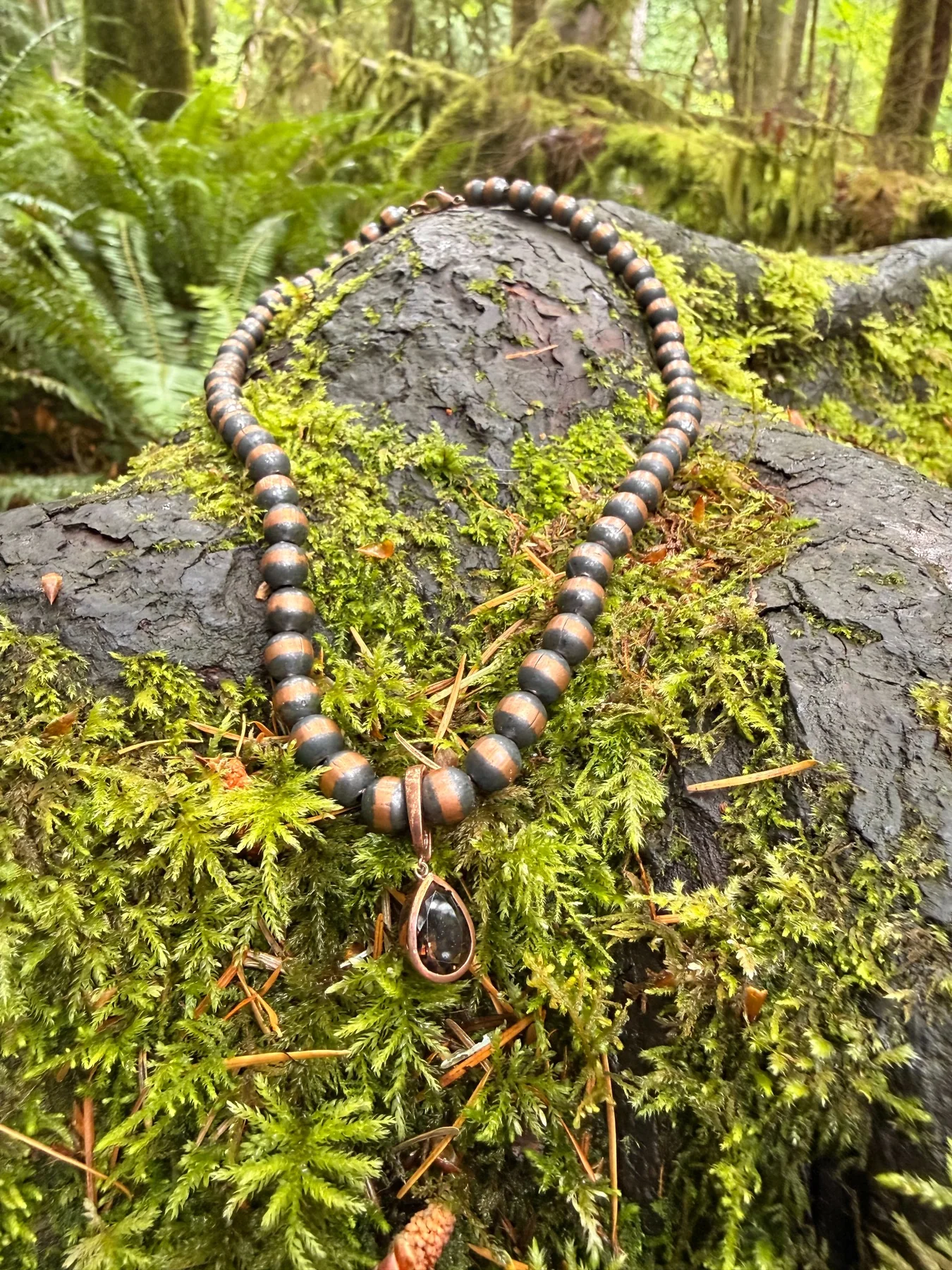 Necklace with a dark teardrop pendant displayed on moss